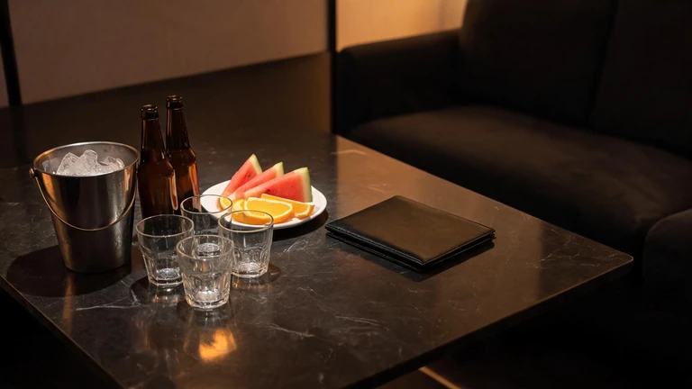 包廂茶几近景：冰桶、啤酒、玻璃杯、水果盤與一個闔起來的皮革帳單夾